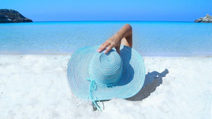 cadeaux-entreprise-vacances-ete personne allongée sur une plage qui tient son chapeau bleu sur sa tête