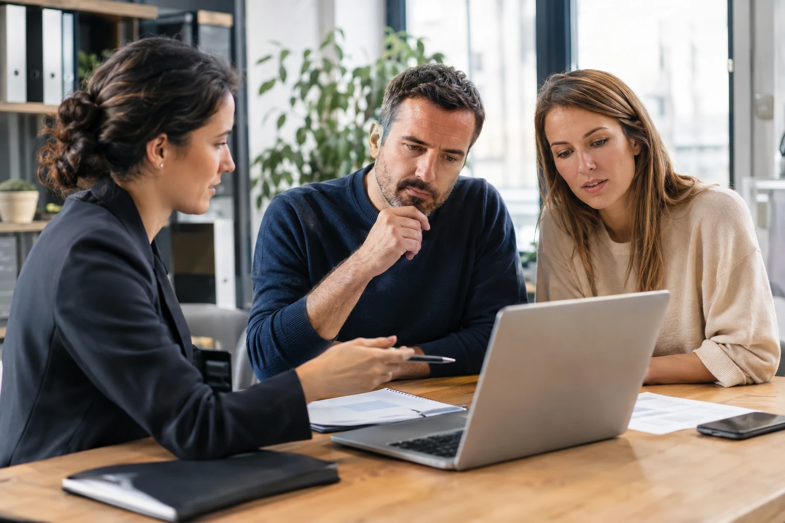 Conseillère présente documents et laptop à un couple attentif dans bureau lumineux