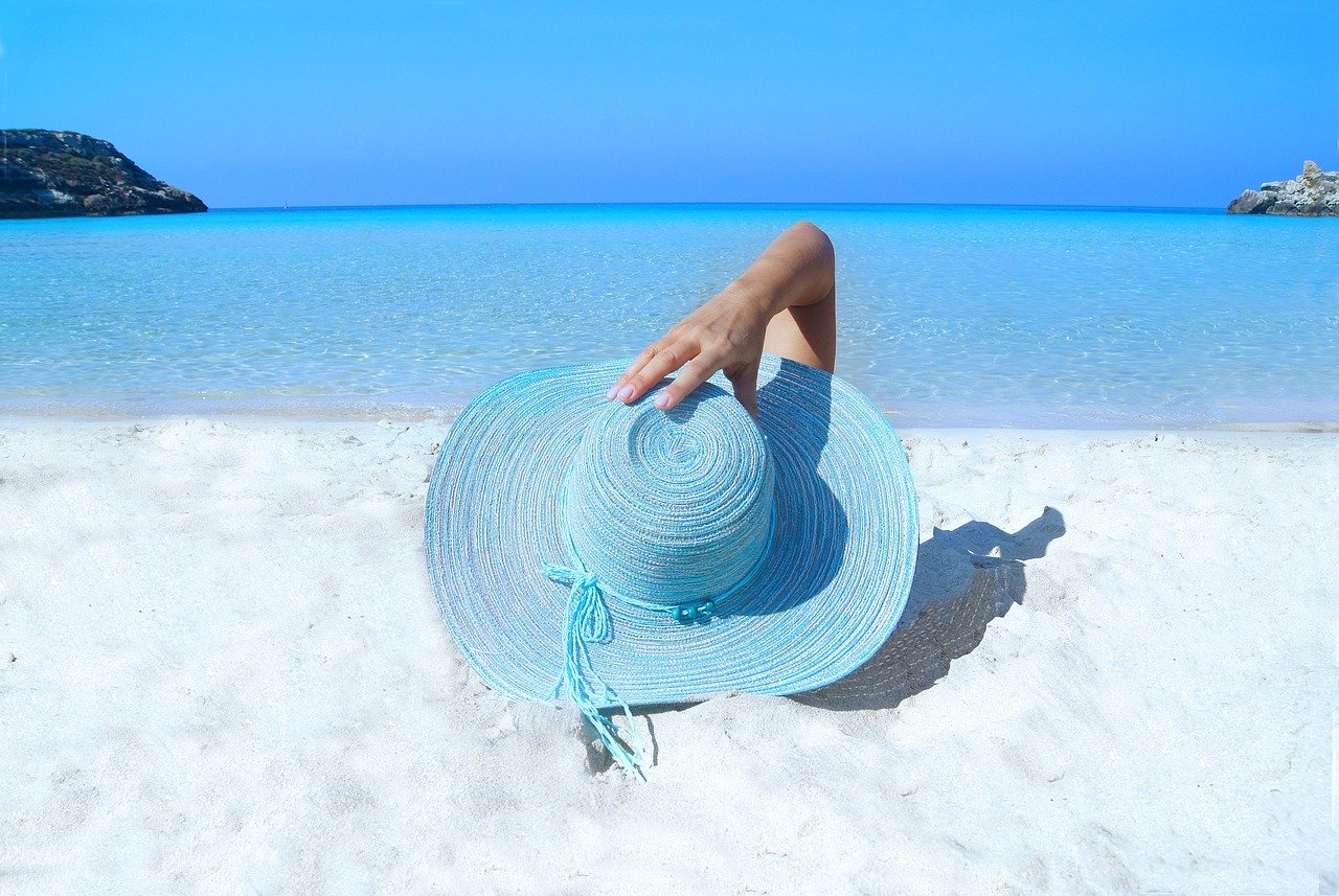 personne allongée sur une plage qui tient son chapeau bleu sur sa tête